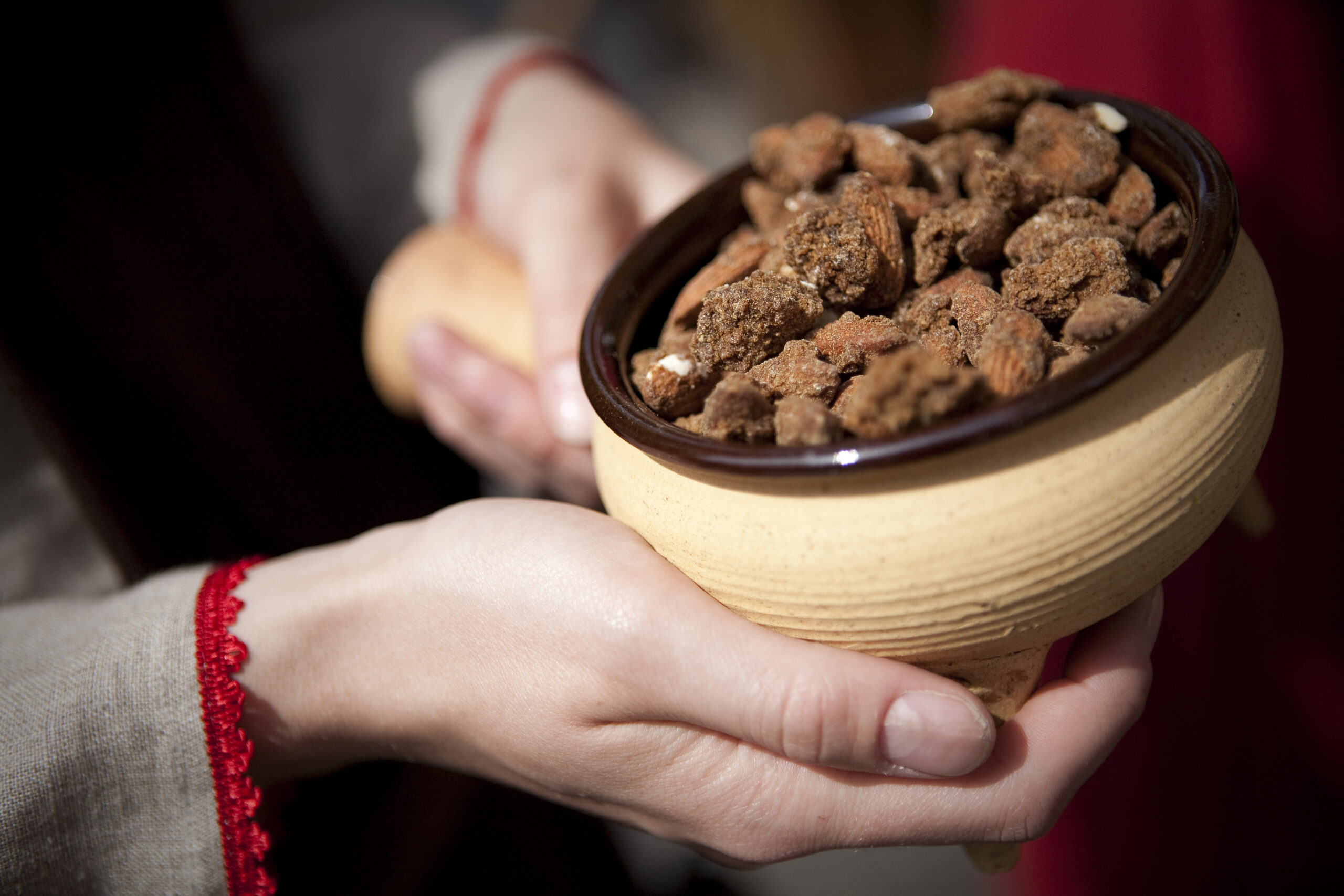 Two hands holding a clay bowl of honeyed almonds
