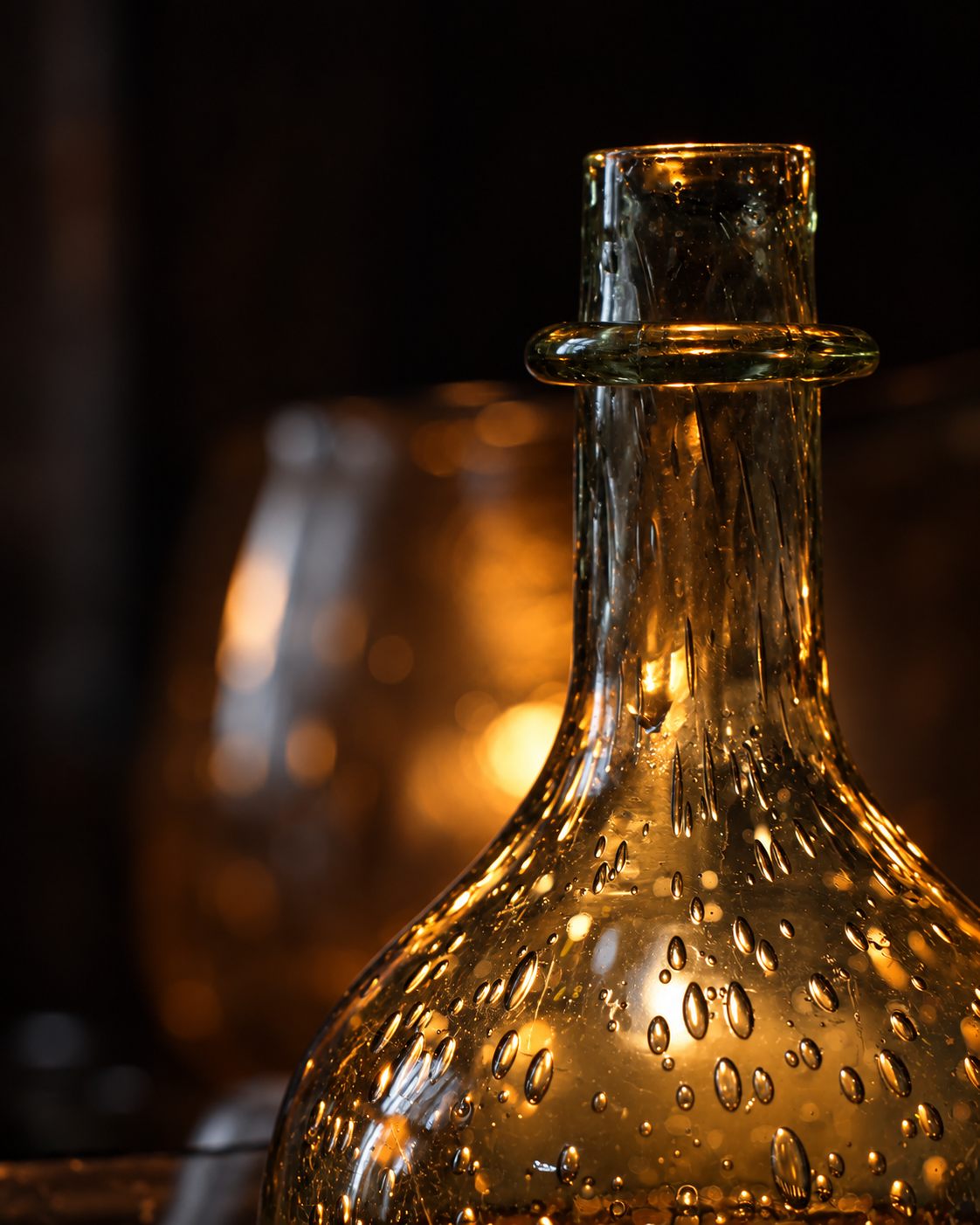 A hand-blown glass bottle full of air bubbles, lit by candlelight