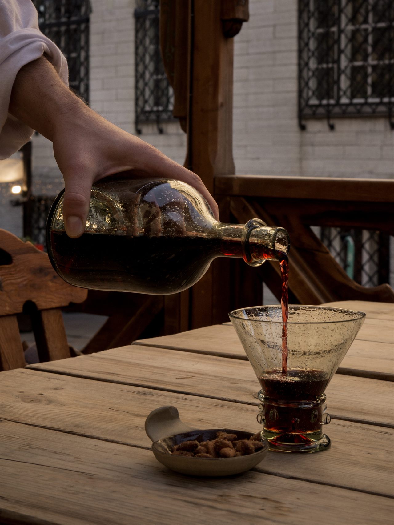Red wine poured from a glass bottle into a forest-glass beaker on a wooden table